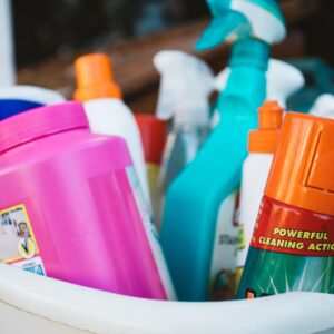 Close-up of assorted cleaning supplies in a bucket outdoors, showcasing various detergents and sprays.
