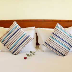 Elegant hotel bed setting with striped pillows and a red rose for a touch of romance.