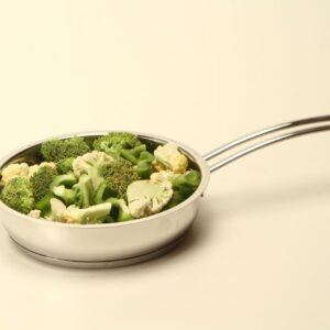 Healthy broccoli and cauliflower florets in a stainless steel pan on a plain background.