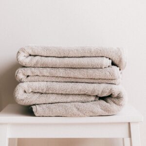 Stack of soft clean light beige folded towels placed on white minimalist stool against beige wall in daylight